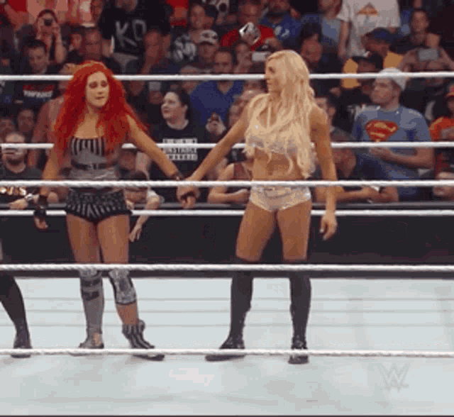 two women in a wrestling ring with a man in a superman shirt in the crowd