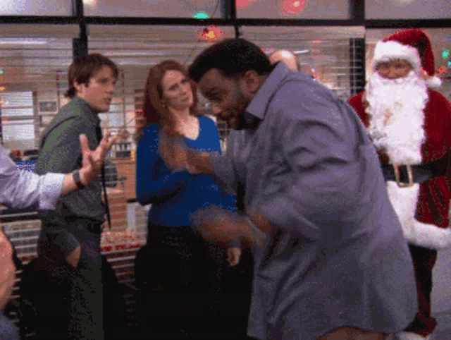 a man in a gray shirt is dancing in front of santa claus