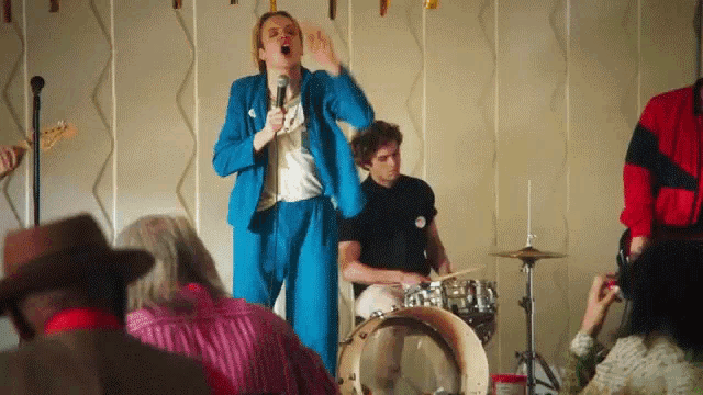 a woman in a blue suit sings into a microphone while a man plays drums