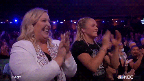 two women are applauding in a crowd with the nbc logo on the bottom right