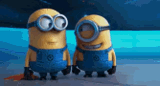 a couple of minions standing next to each other on a beach .
