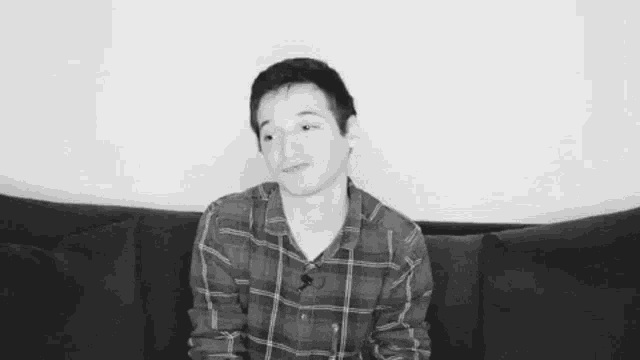 a man in a plaid shirt is sitting on a couch .