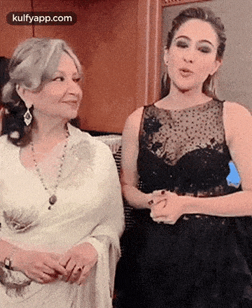 two women are standing next to each other in a room and smiling .