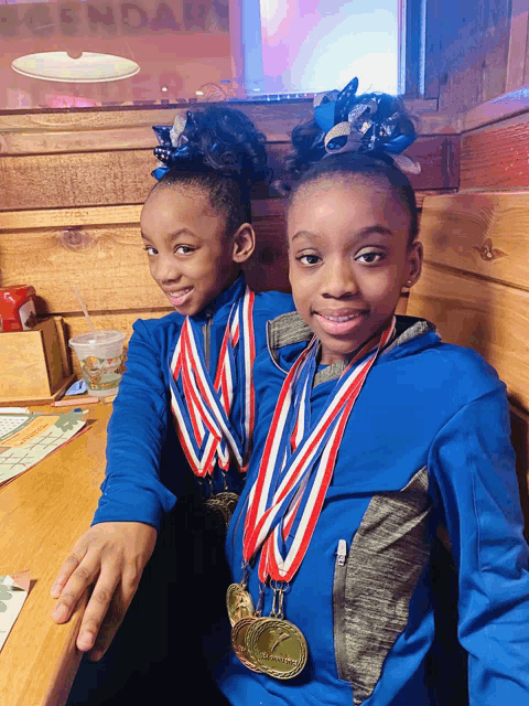 two girls wearing medals are sitting at a table with a sign that says legendary