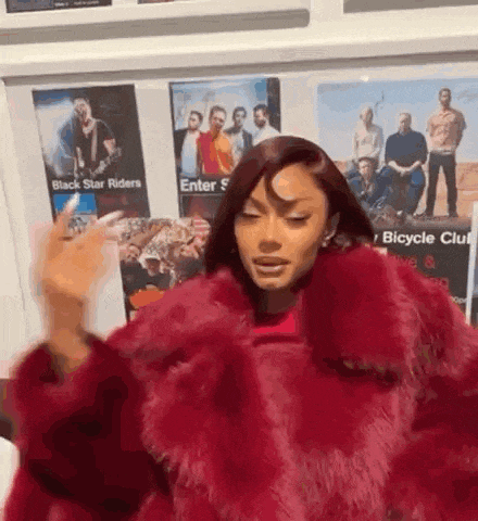 a woman in a red fur coat is standing in front of a wall with posters on it .