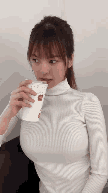 a woman in a white turtleneck is drinking from a cup that says mcdonald 's on it