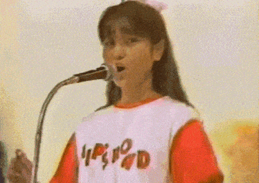 a girl singing into a microphone wearing a red and white shirt that says lp & d on it