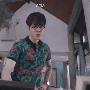 a man wearing glasses and a floral shirt is standing in a room with shia written on the bottom