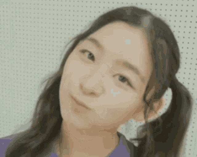a young girl with pigtails is making a funny face with her hand to her face .