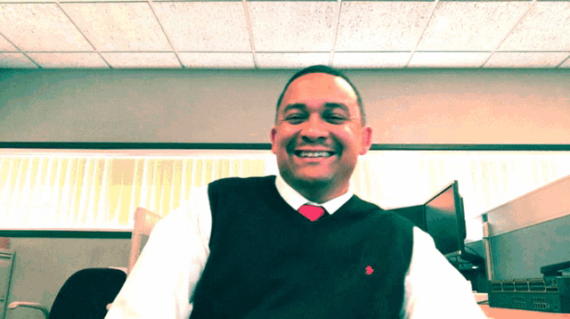 a man wearing a black vest and a red tie smiles at the camera
