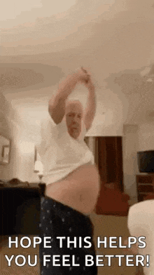 a man with a very large belly is standing in a living room with his arms in the air .