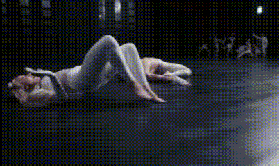 a woman is laying on the floor in a dark room with a group of people standing in the background .
