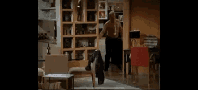 a man is standing in a living room in front of a bookshelf and chairs .