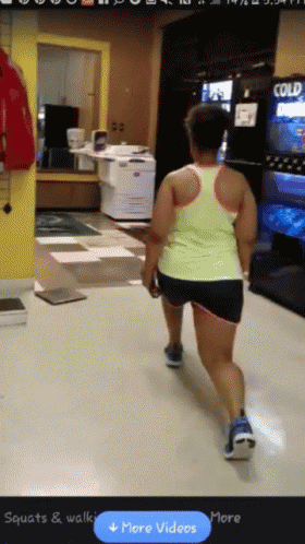 a woman in a yellow tank top is walking down a hallway with a blue button that says more videos