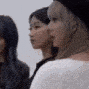 three women are standing next to each other and looking at something . one of the women is wearing a black hat .