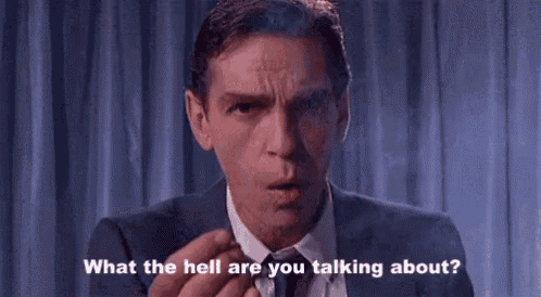 a man in a suit and tie is smoking a cigarette and saying `` what the hell are you talking about '' .