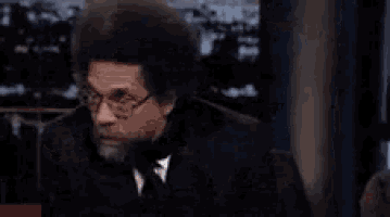 a man with a beard and glasses is pointing at something with the words oh my behind him .