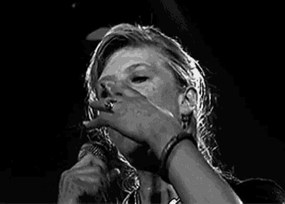 a black and white photo of a woman singing into a microphone on a stage .