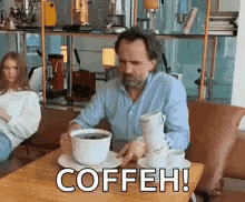a man is sitting at a table with a stack of coffee cups on it .