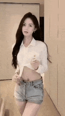 a woman wearing a white shirt and denim shorts is standing in a room .