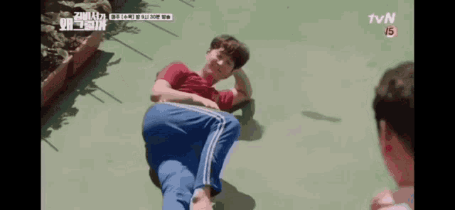 a man in a red shirt and blue pants is laying on the ground while another man looks on .