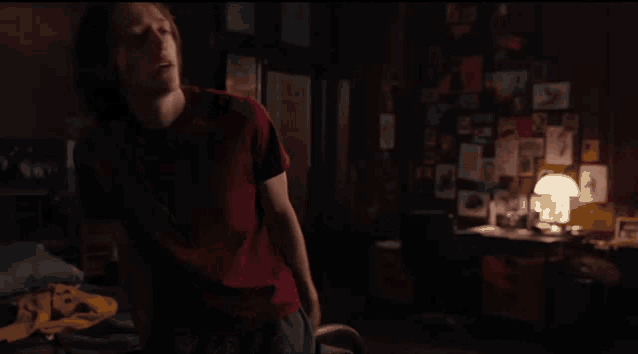 a man in a red shirt is standing in a dark room with posters on the wall