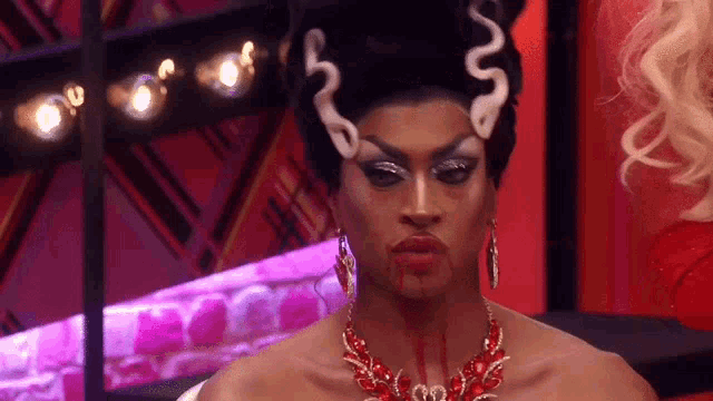 a drag queen with blood on her face is wearing a necklace