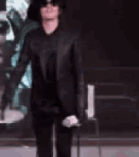 a man in a black suit and hat is holding a microphone
