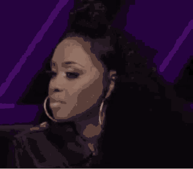 a woman wearing hoop earrings and a bun is sitting in a chair .