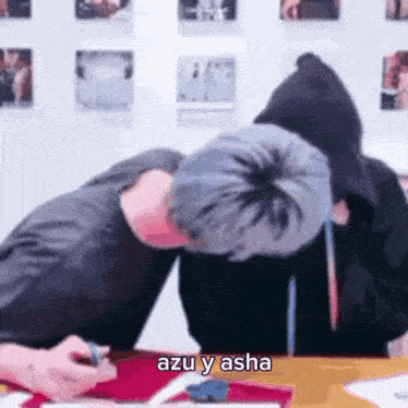two men are sitting at a table with their heads on each other . one of them is wearing a hoodie .