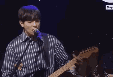 a man is playing a guitar and singing into a microphone on stage .
