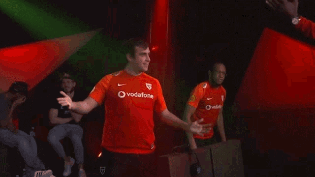a man wearing a red vodafone shirt hugs another man