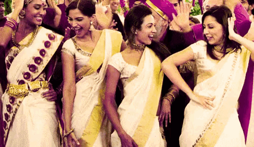 a group of women in white and yellow saris are dancing