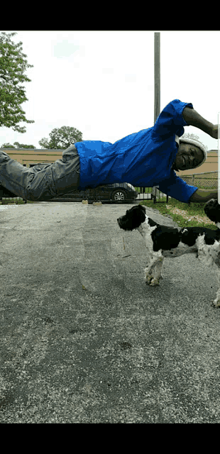 a man in a blue shirt is laying on the ground next to a black and white dog