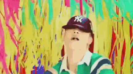 a person wearing a baseball cap and a green shirt is standing in front of a colorful wall .