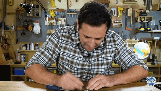 a man in a plaid shirt is using a screwdriver in a workshop with the word mundo on the bottom