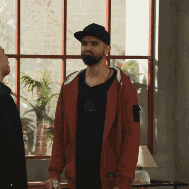 a man with a beard wearing a black hat and a red hoodie