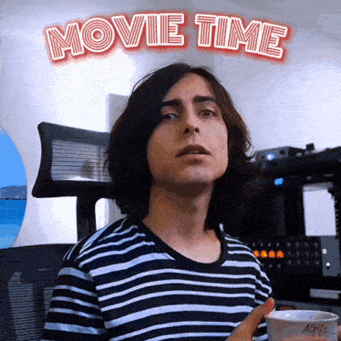 a man in a striped shirt is standing in front of a sign that says " movie time "