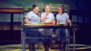 three women are standing around a table with bowls of food