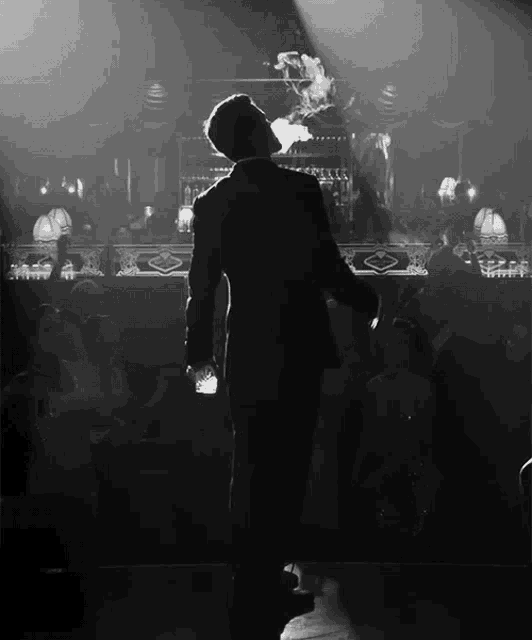 a man in a suit stands in front of a crowd smoking a cigar