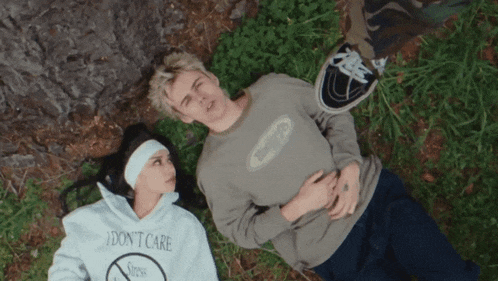 a man and a woman are laying in the grass and the woman is wearing a shirt that says i don t care