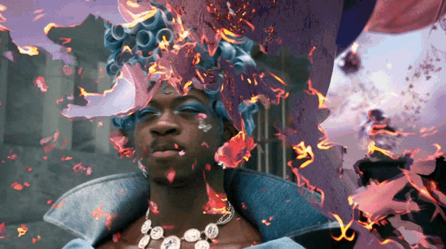 a man wearing a blue wig and a necklace is surrounded by flames
