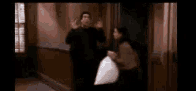 a man and a woman are standing next to each other in a hallway . the woman is holding a white bag .