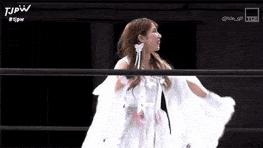 a woman is standing in a wrestling ring wearing a white dress .