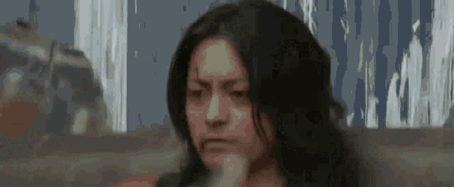 a woman with long dark hair is looking at the camera with a serious look on her face .
