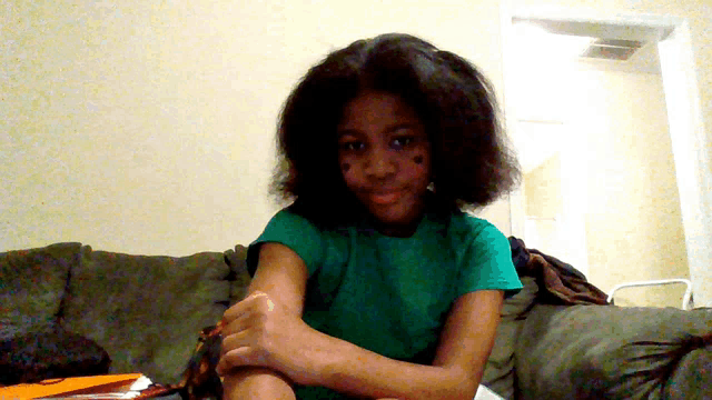 a girl in a green shirt sits on a couch with her arms crossed