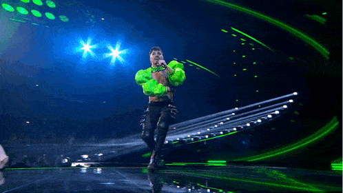 a man in a neon green jacket is singing into a microphone on a stage