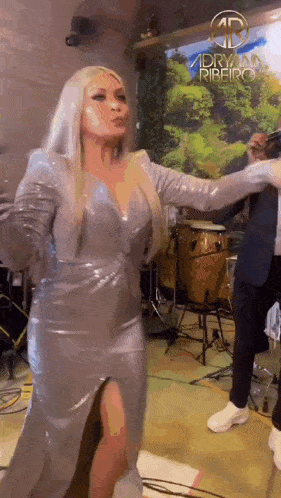 a woman in a silver dress is dancing on a stage in front of a drummer .