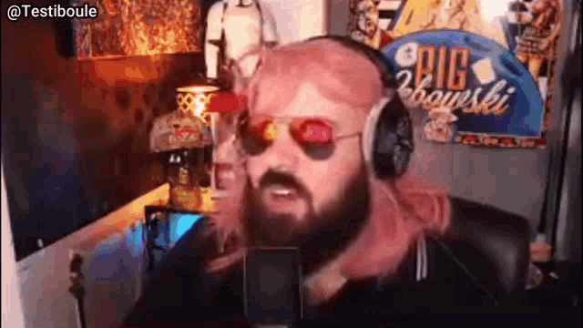a man with a beard wearing headphones and sunglasses is talking into a microphone .