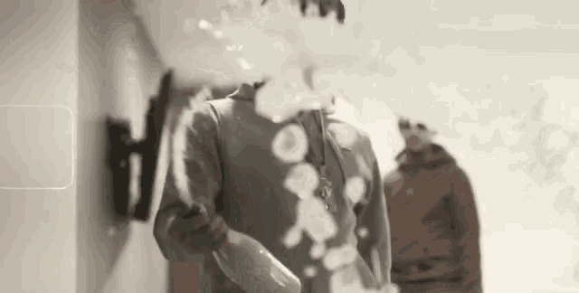a man is blowing soap bubbles in a hallway while another man stands behind him .